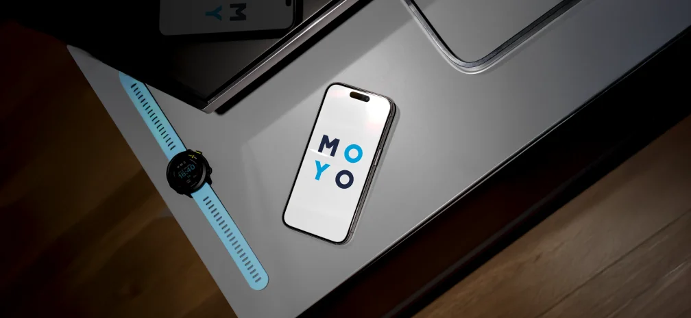 Смартфон із логотипом MOYO на екрані поруч із годинником