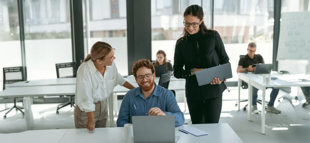 A marketing team gathered around a laptop discussing campaign results in a modern office.