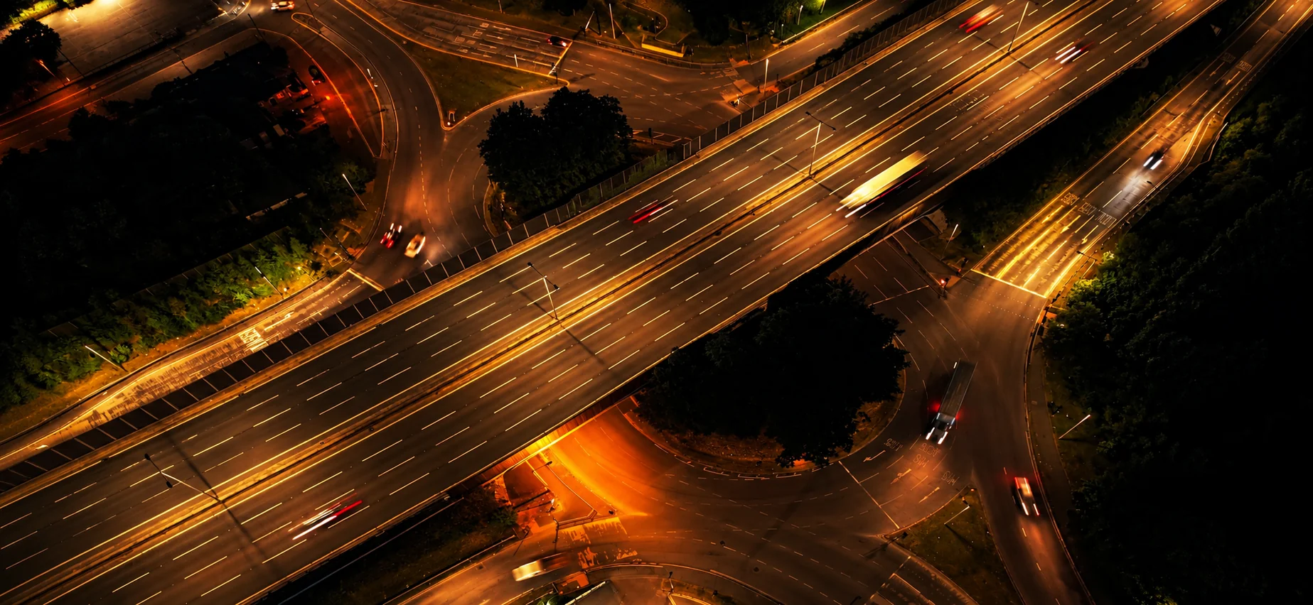 Aerial view of a highway interchange at night with illuminated roads and moving traffic.