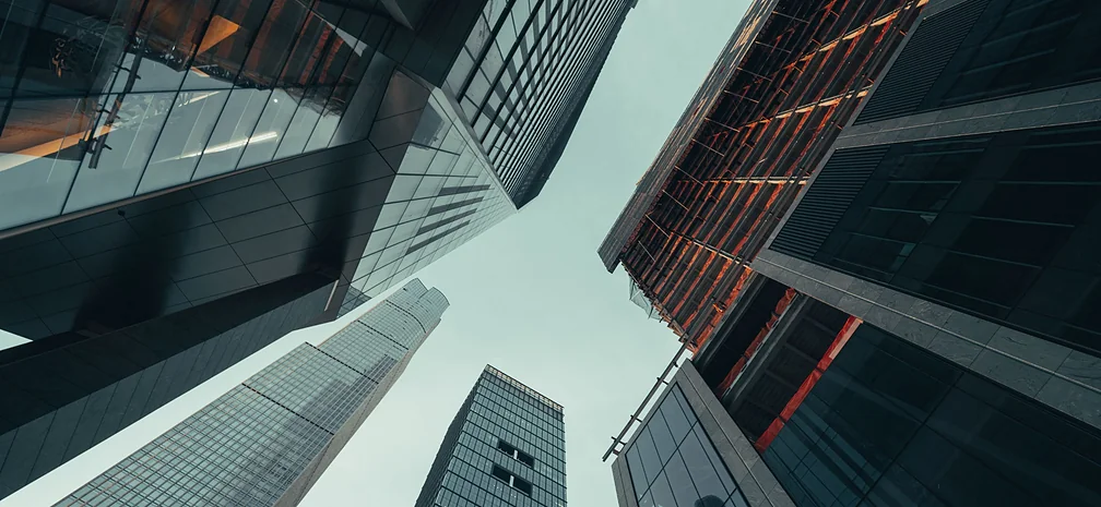 Low-angle view of modern glass skyscrapers rising into a cloudy sky.